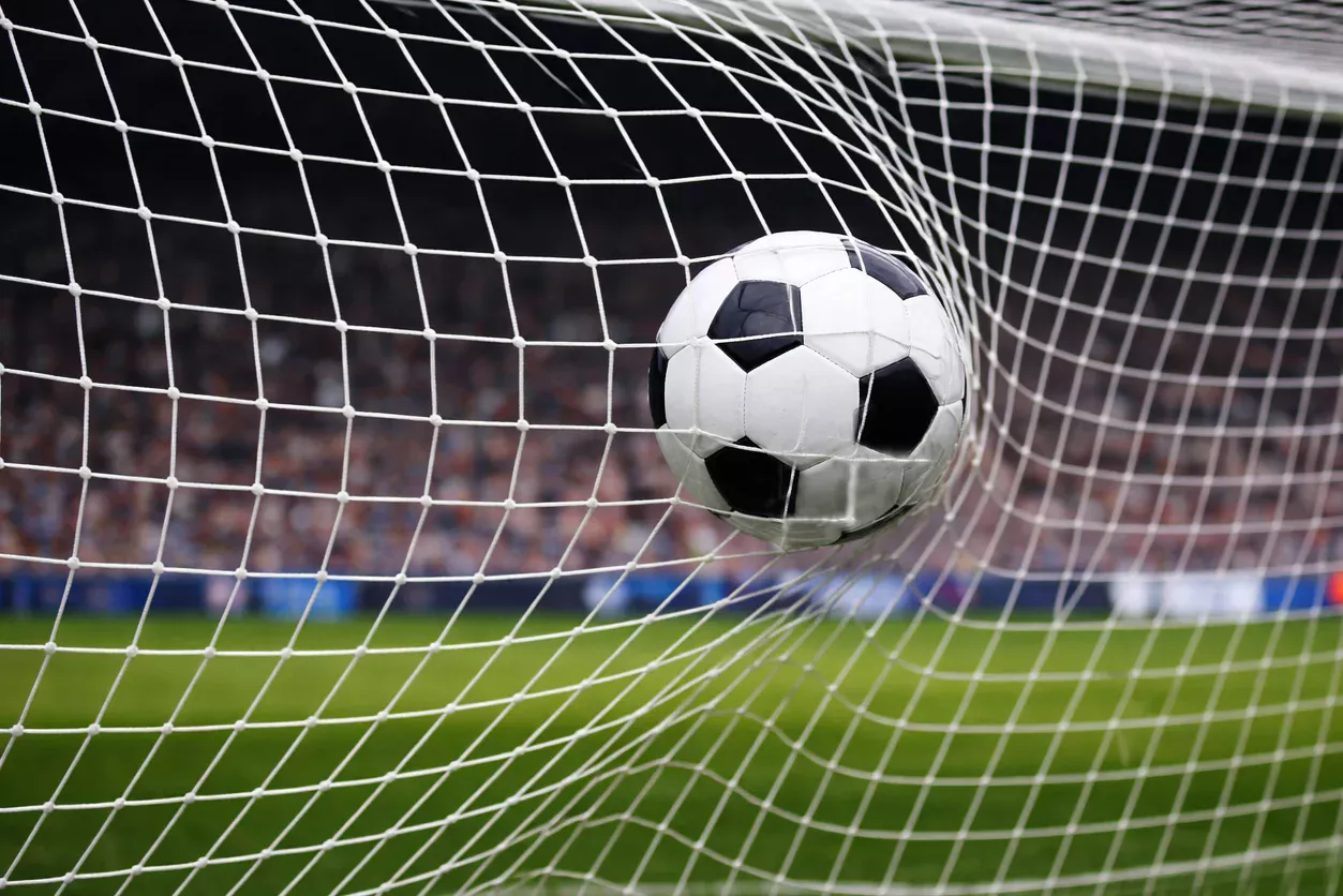 Balón de fútbol entrando en la red de una portería en un estadio iluminado