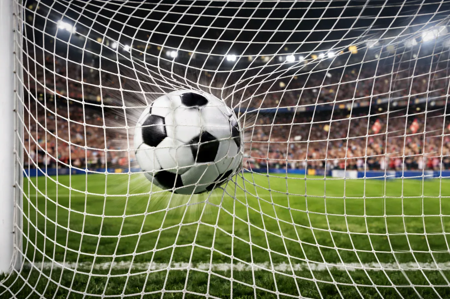 Balón de fútbol entrando en la portería en un estadio lleno de aficionados celebrando un gol